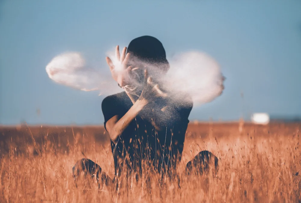 Person outdoors blowing powder or smoke into the air