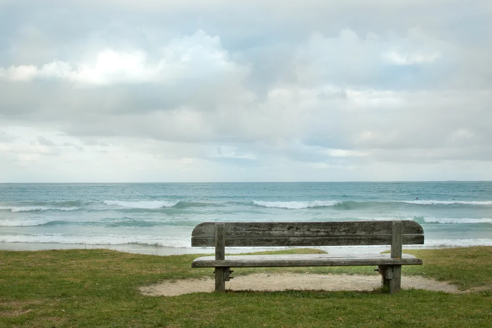 Empty bench overlooking the ocean under cloudy skies.