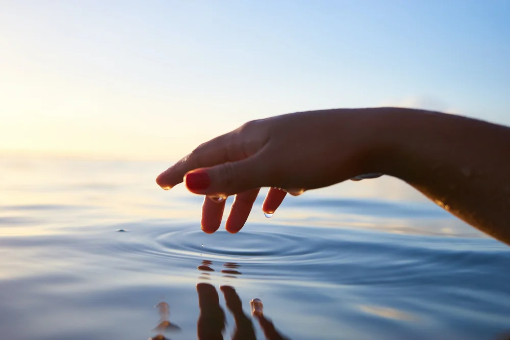 Hand touching calm water at sunset